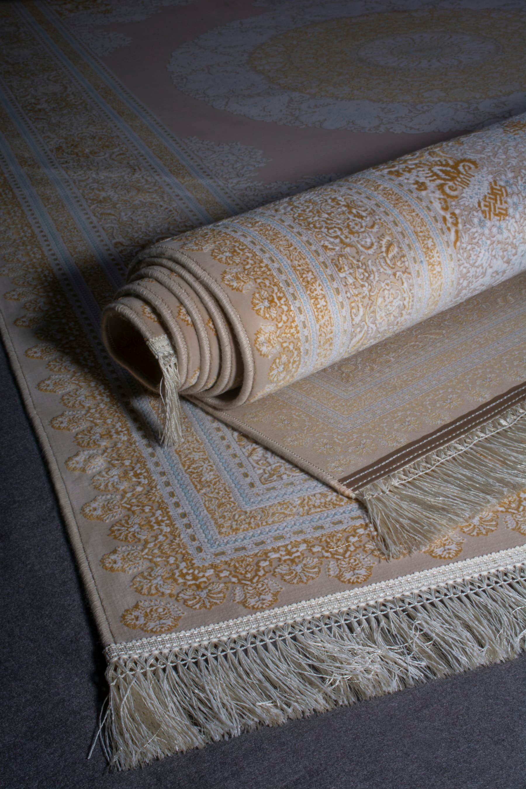 A cream and gold patterned rug with a rolled edge and fringe