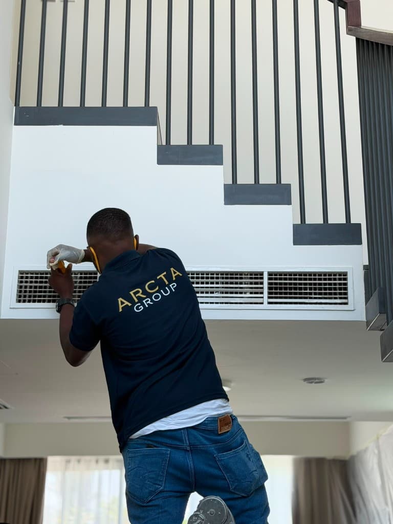 Arcta Group technician in uniform servicing a ceiling air-conditioning vent